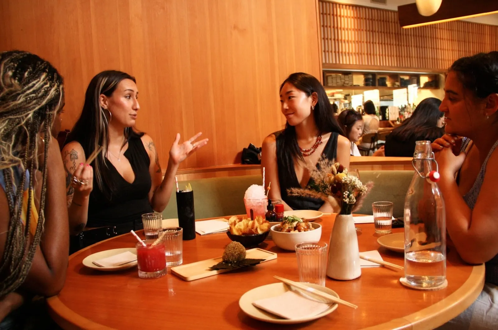 four guests mid-conversation over shared plates and cocktails